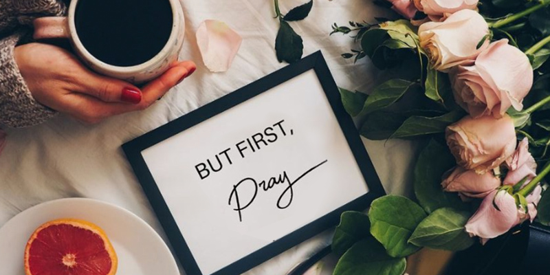 Woman holding mug, flowers, fruit and frame that says But First, Pray