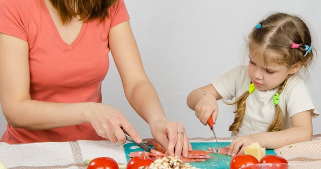Little girl cutting chicken with mom